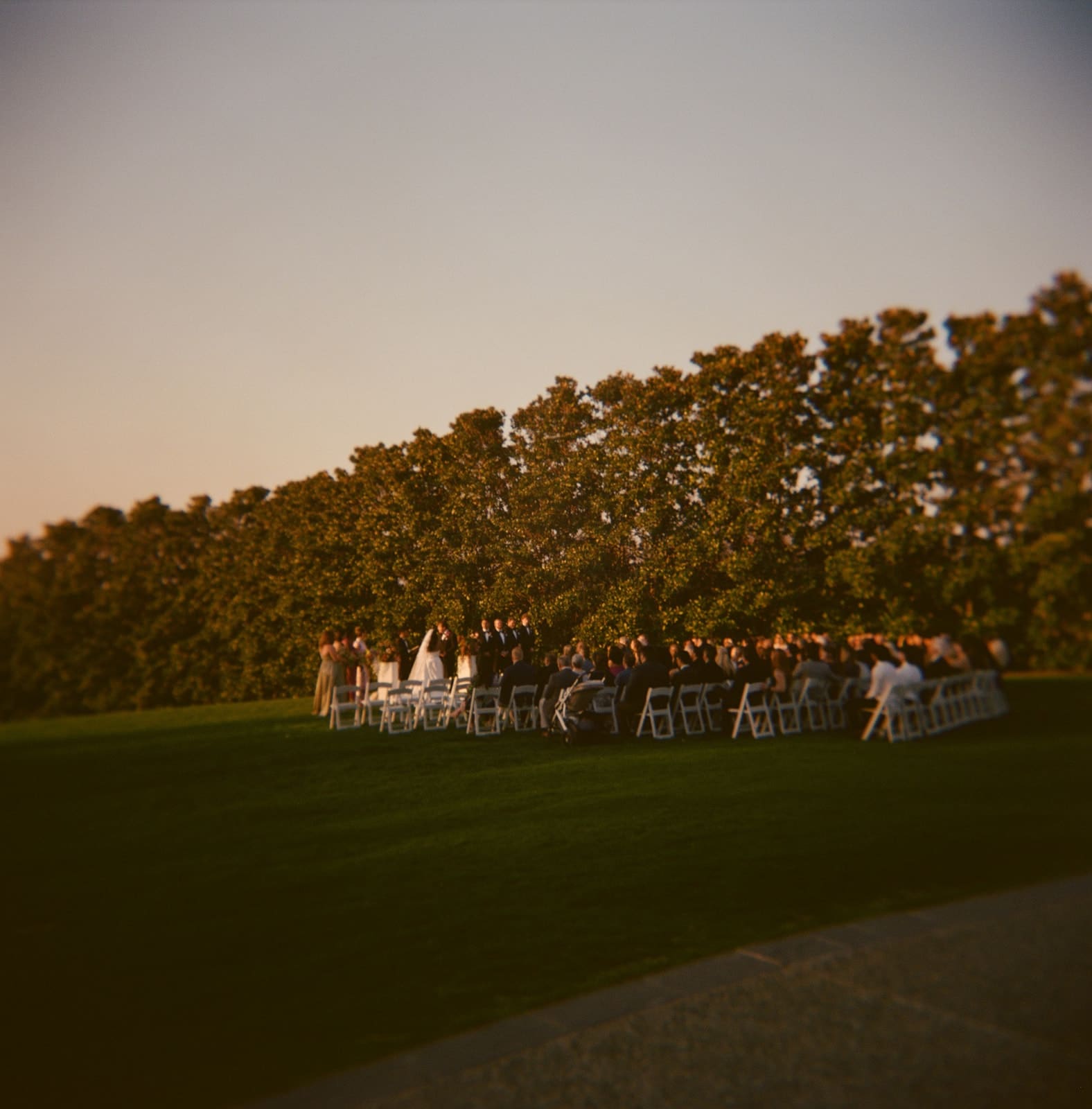 Outdoor wedding ceremony by a lake at sunset, with guests seated on both sides and a couple standing at the altar at a Dallas Arboretum Wedding