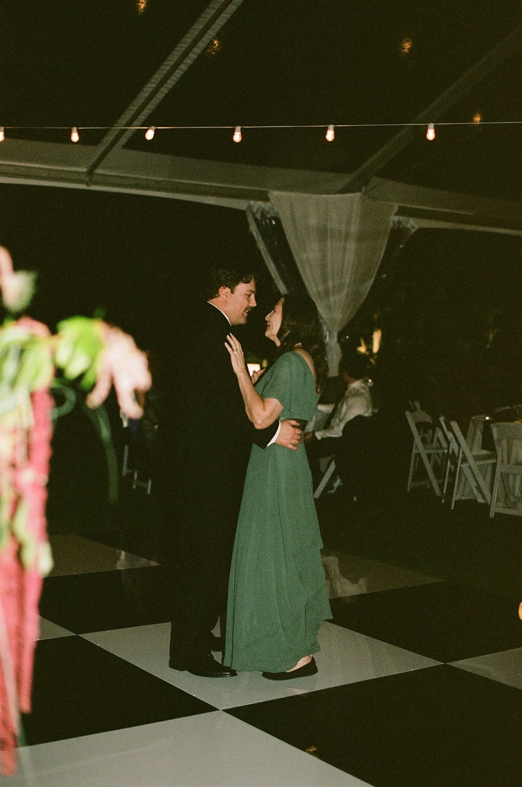 A bride in a white dress and guests in formal attire dance together at a lively indoor celebration for a Dallas Arboretum Wedding