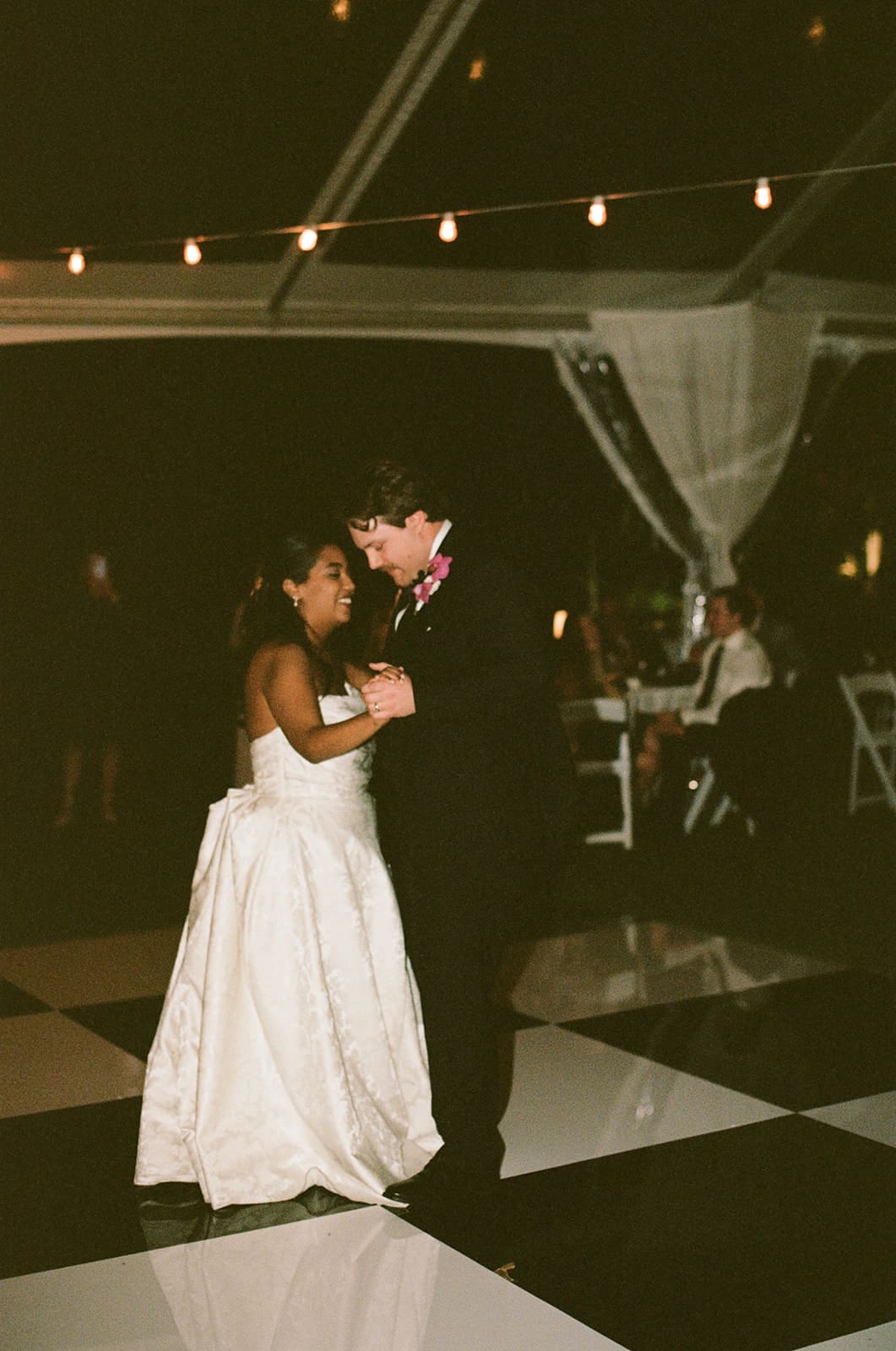 A bride in a white dress and guests in formal attire dance together at a lively indoor celebration for a Dallas Arboretum Wedding
