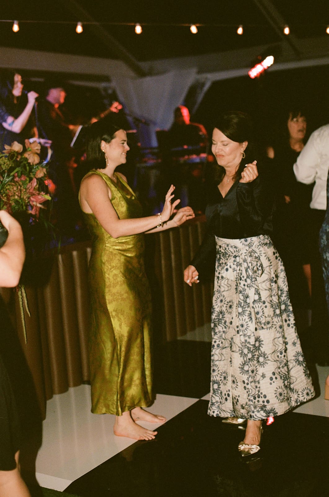 A bride in a white dress and guests in formal attire dance together at a lively indoor celebration for a Dallas Arboretum Wedding