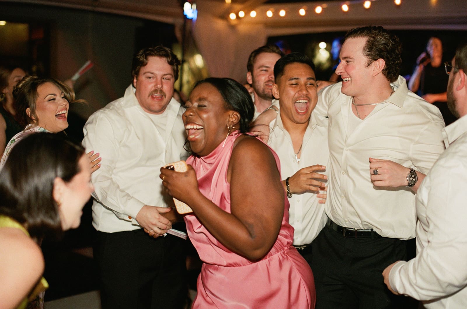 A group of people, dressed in formal attire, laugh and celebrate together at an indoor event or party.