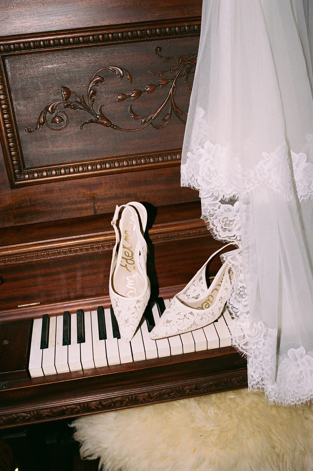 A pair of white lace high-heeled shoes resting on piano keys, with part of a lace-trimmed white dress draped nearby.