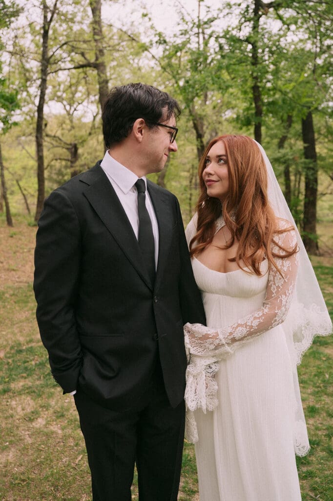 A bride and groom stand facing each other outdoors, holding hands, with an officiant reading between them during a wedding ceremony at An Intimate Backyard Wedding in Dallas