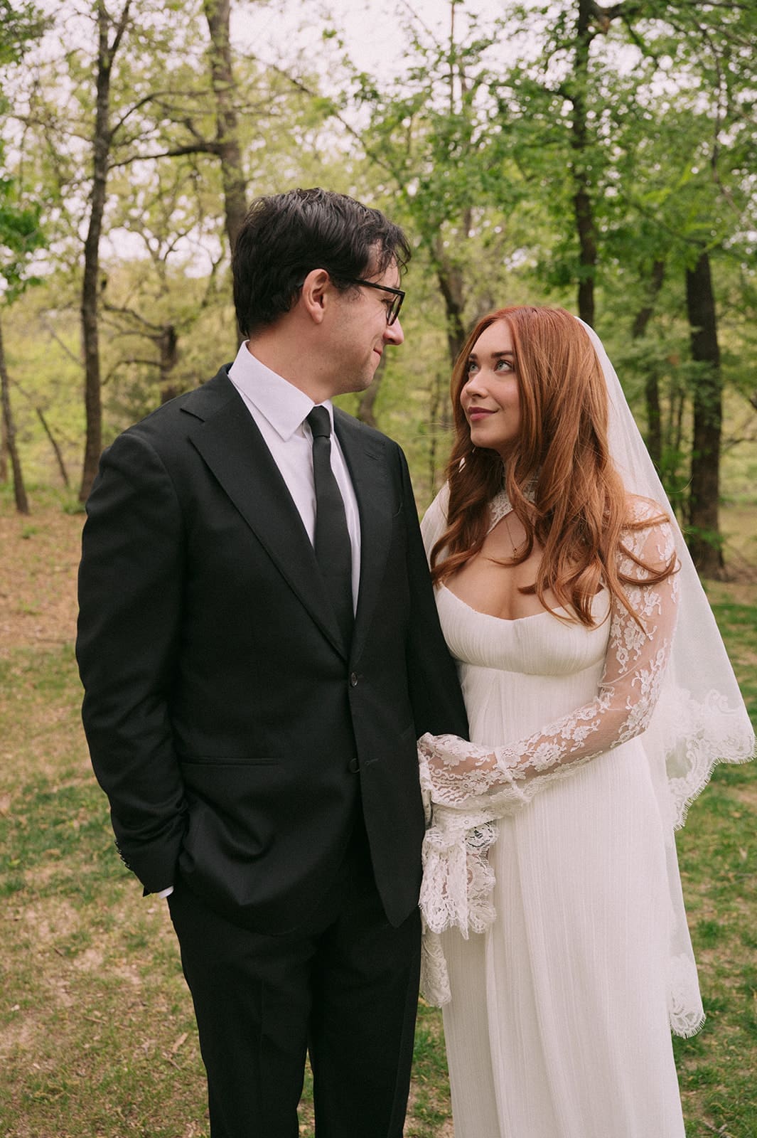 A bride and groom stand facing each other outdoors, holding hands, with an officiant reading between them during a wedding ceremony at An Intimate Backyard Wedding in Dallas
