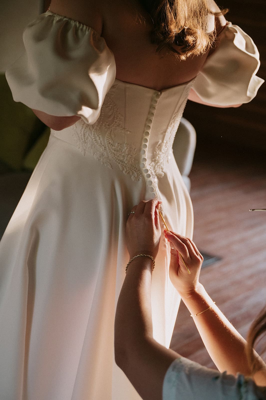 A woman in a dress is being assisted by another person in a softly lit room