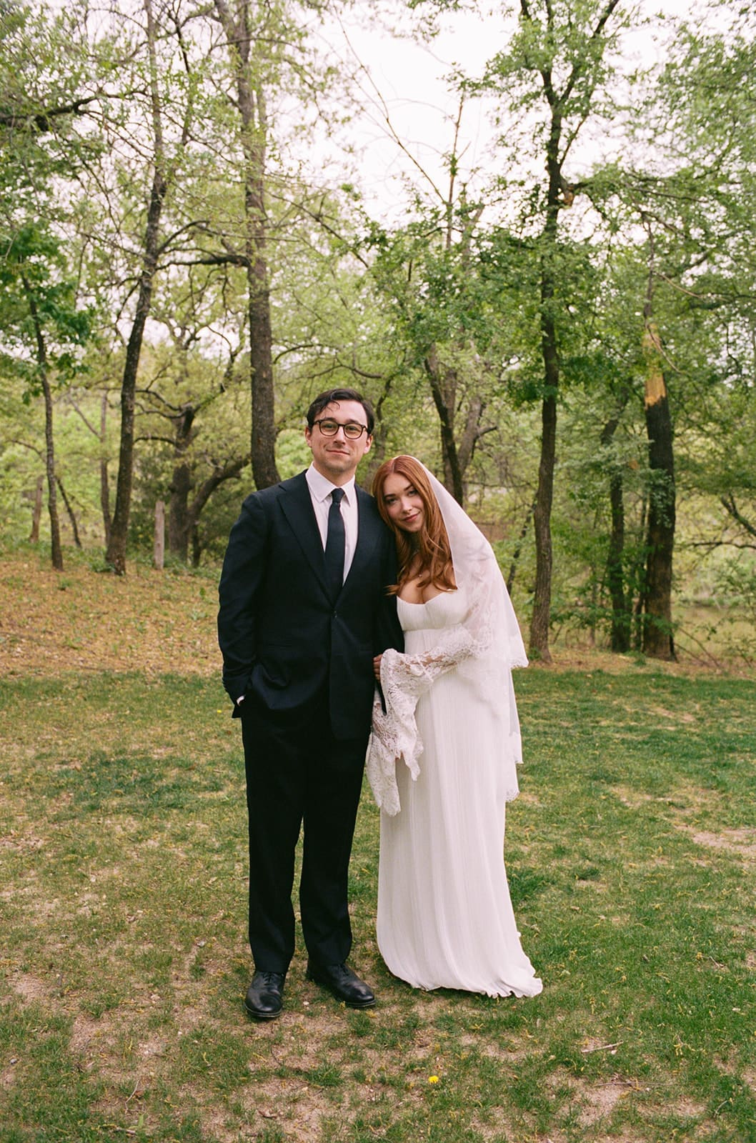 A bride and groom stand facing each other outdoors, holding hands, with an officiant reading between them during a wedding ceremony at An Intimate Backyard Wedding in Dallas