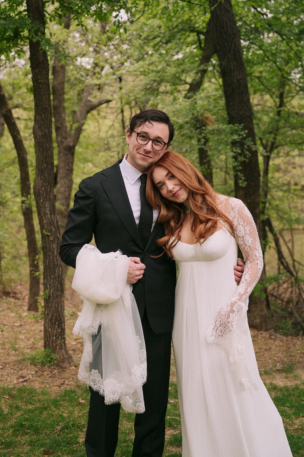 A bride and groom stand facing each other outdoors, holding hands, with an officiant reading between them during a wedding ceremony at An Intimate Backyard Wedding in Dallas