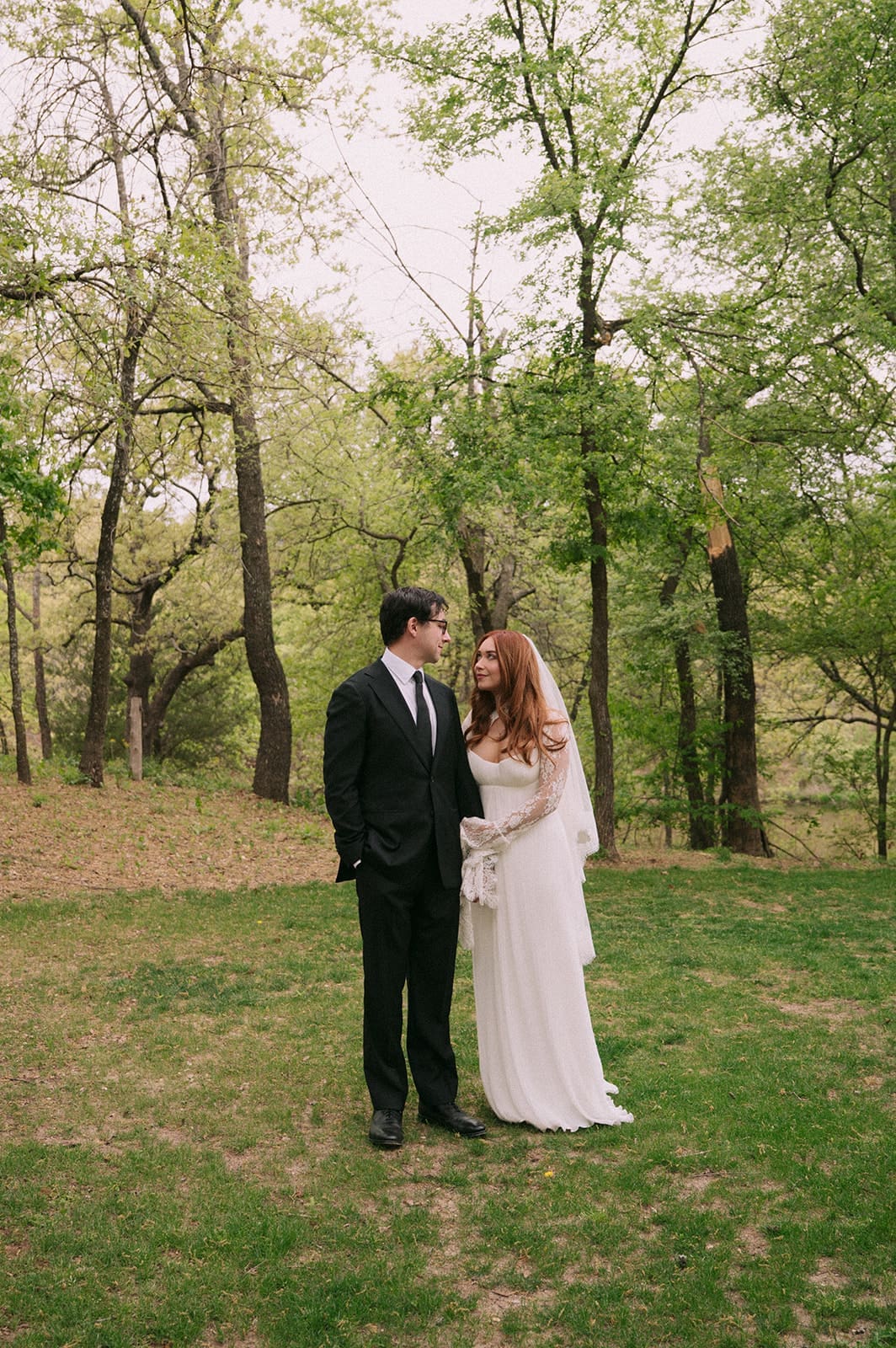 A bride and groom stand facing each other outdoors, holding hands, with an officiant reading between them during a wedding ceremony at An Intimate Backyard Wedding in Dallas