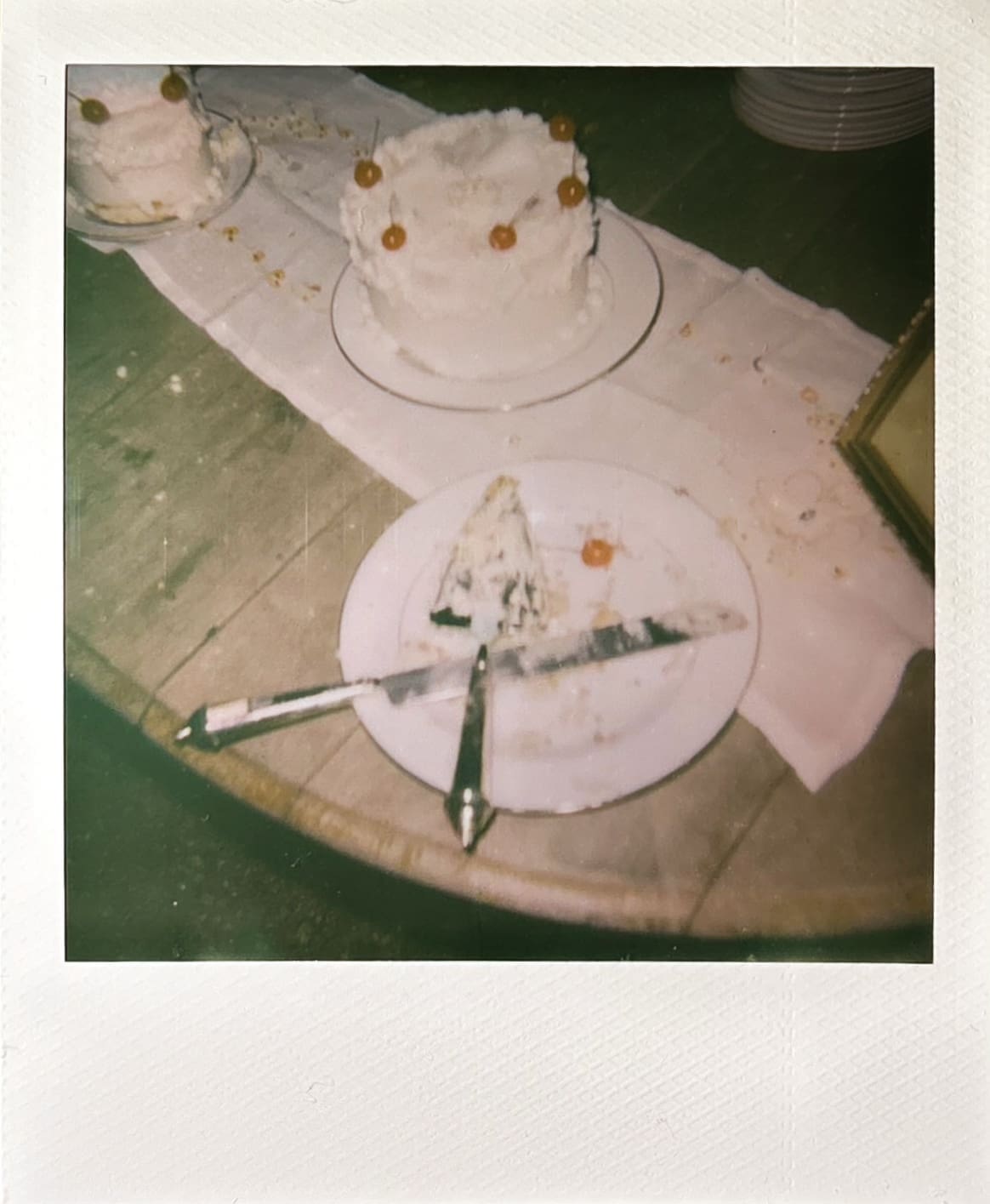 A couple in formal attire stands together cutting a tiered cake, with bowls and a framed photo on the table beside them.