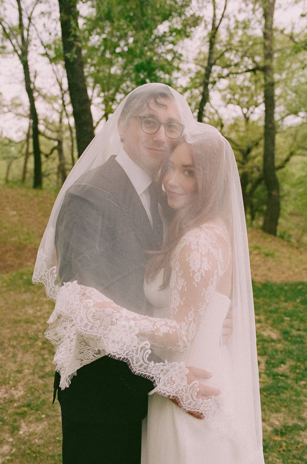 A bride and groom stand facing each other outdoors, holding hands, with an officiant reading between them during a wedding ceremony at An Intimate Backyard Wedding in Dallas
