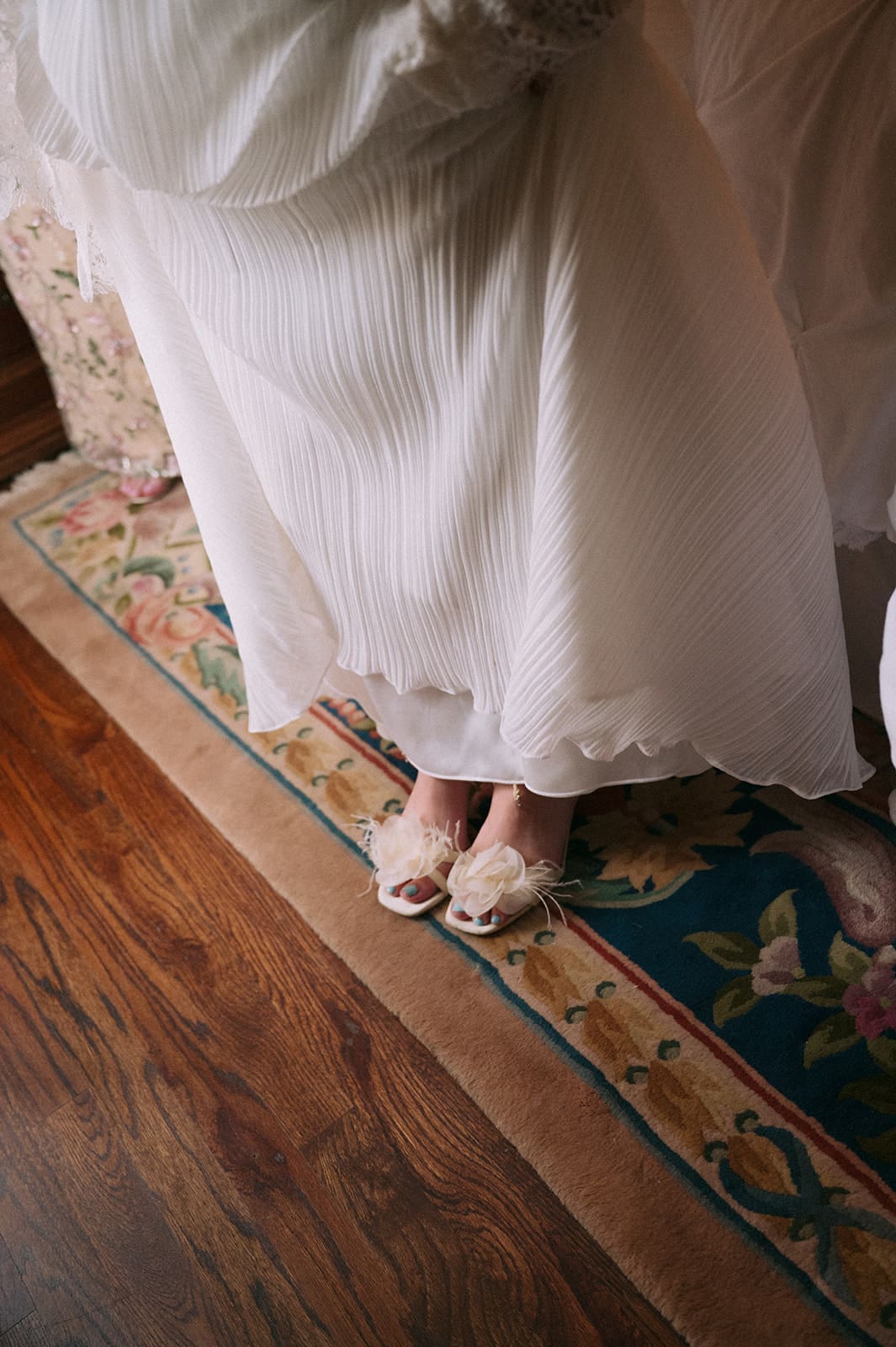 Person wearing a white dress and open-toed shoes standing on a floral rug with hardwood floor visible.