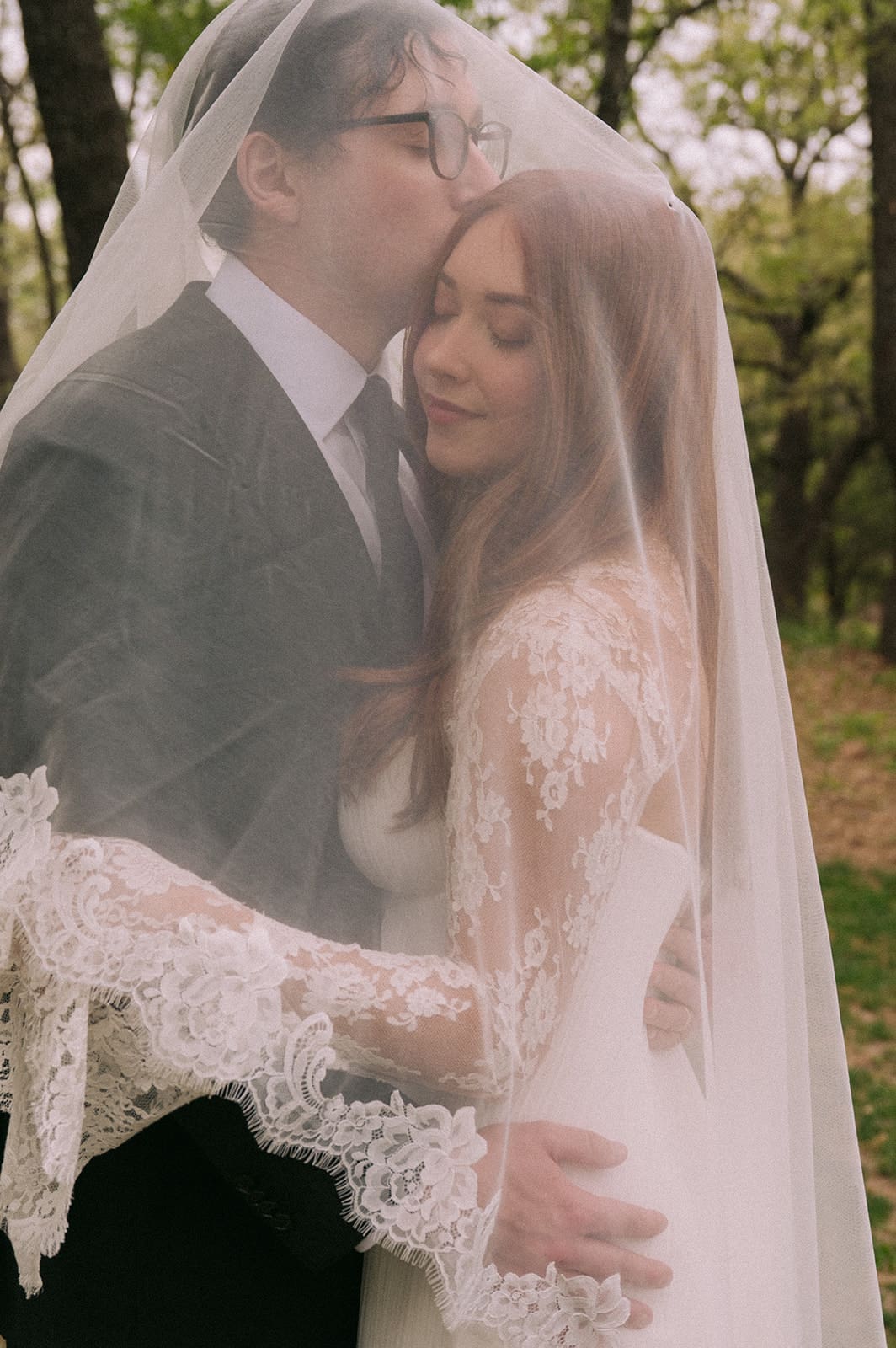 A bride and groom stand facing each other outdoors, holding hands, with an officiant reading between them during a wedding ceremony at An Intimate Backyard Wedding in Dallas