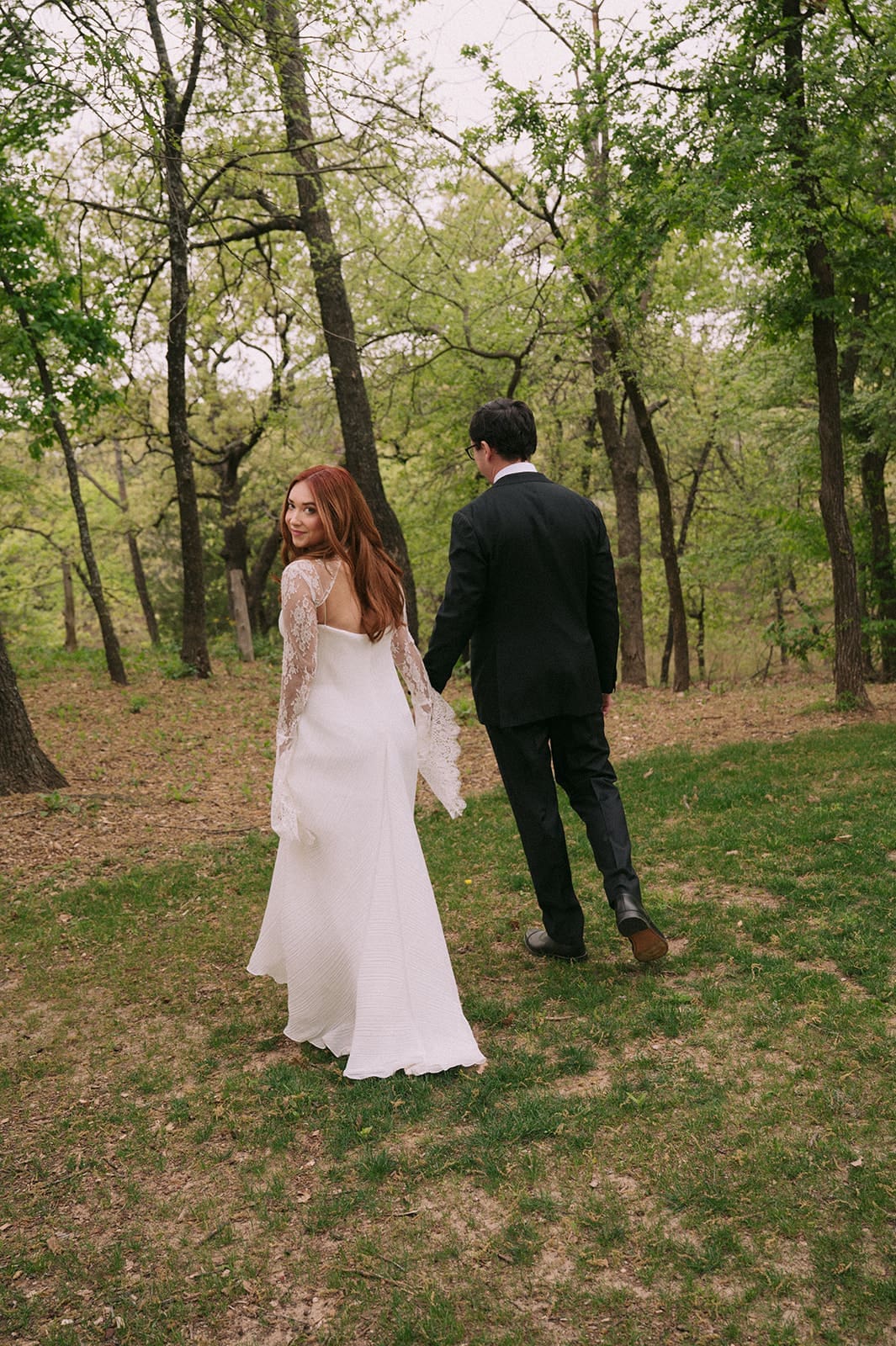 A bride and groom stand facing each other outdoors, holding hands, with an officiant reading between them during a wedding ceremony at An Intimate Backyard Wedding in Dallas