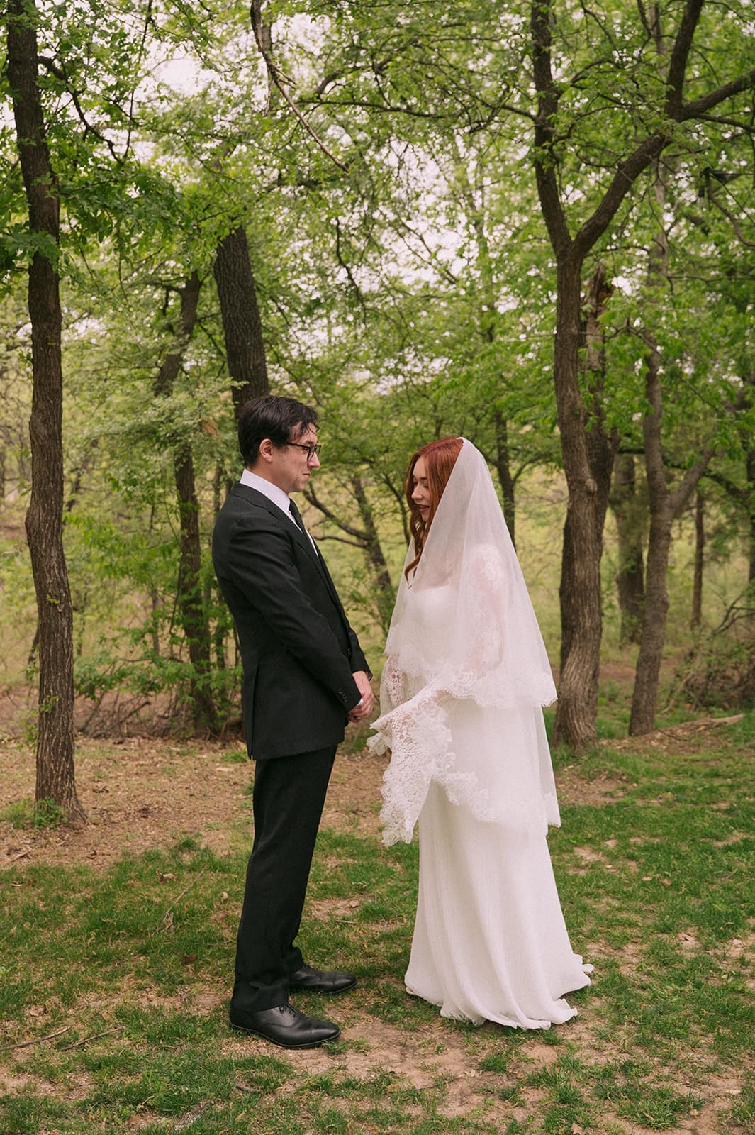 A bride and groom stand facing each other outdoors, holding hands, with an officiant reading between them during a wedding ceremony at An Intimate Backyard Wedding in Dallas