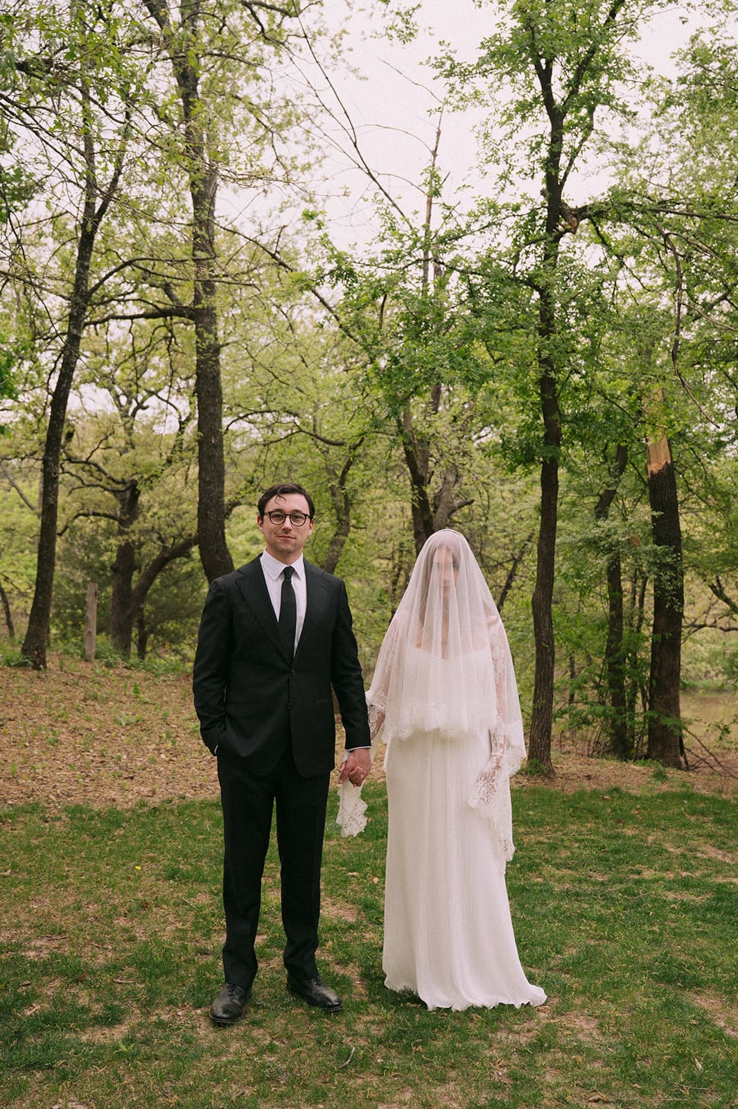 A bride and groom stand facing each other outdoors, holding hands, with an officiant reading between them during a wedding ceremony at An Intimate Backyard Wedding in Dallas