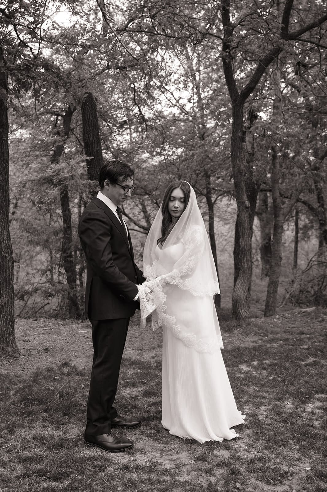 A bride and groom stand facing each other outdoors, holding hands, with an officiant reading between them during a wedding ceremony at An Intimate Backyard Wedding in Dallas