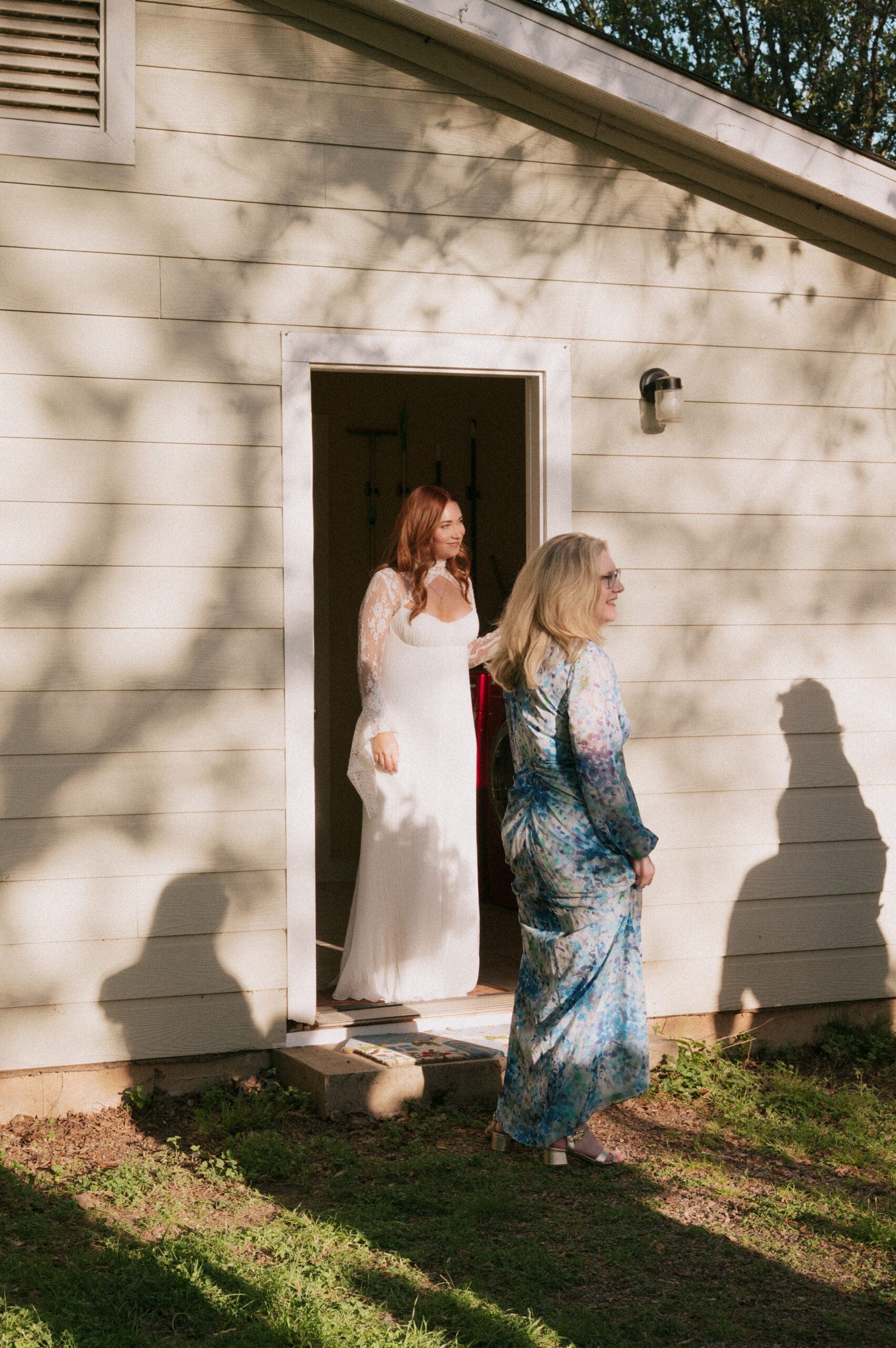 A bride and groom stand facing each other outdoors, holding hands, with an officiant reading between them during a wedding ceremony at An Intimate Backyard Wedding in Dallas
