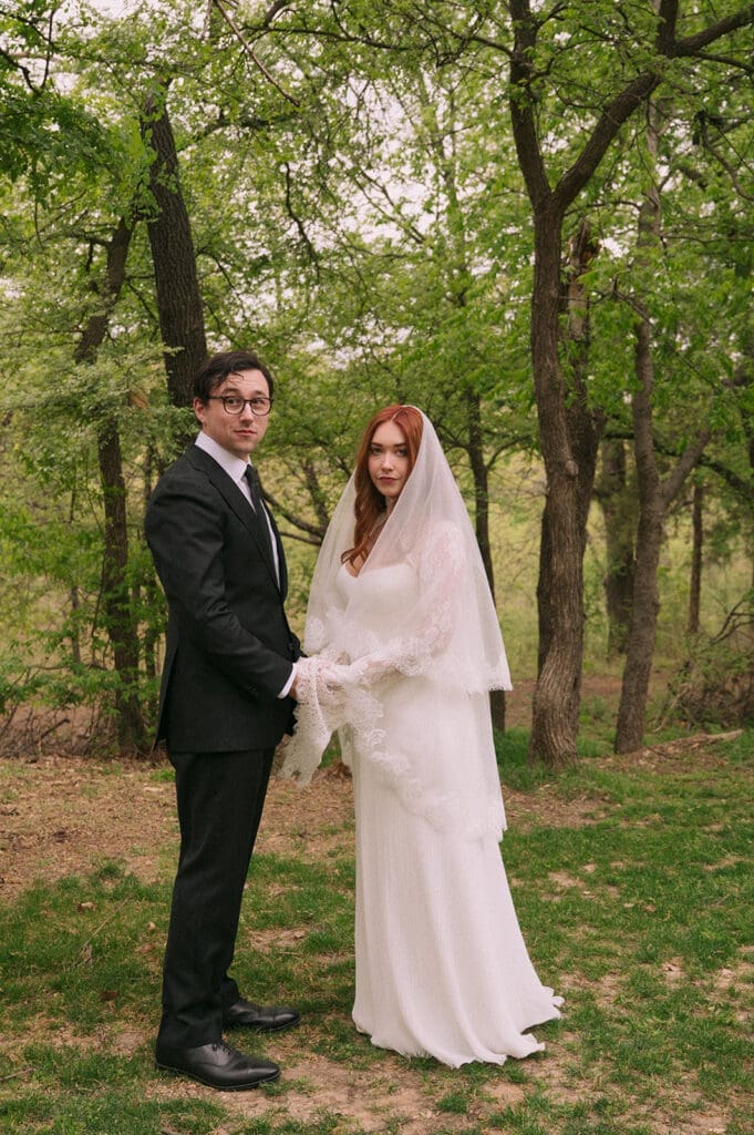 A bride and groom stand facing each other outdoors, holding hands, with an officiant reading between them during a wedding ceremony at An Intimate Backyard Wedding in Dallas