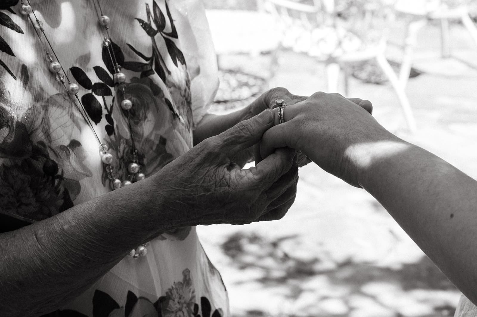 Two people are seen in close-up; one is placing a ring on the other's finger. The scene is outdoors and in black and white.