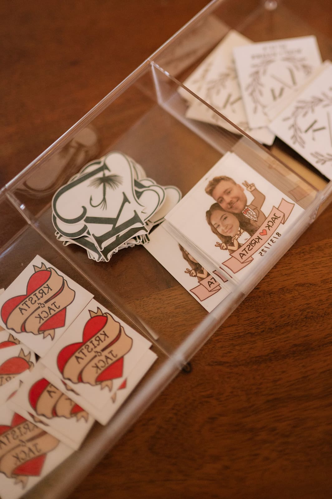 Clear plastic tray on a wooden surface holding paper items, including heart-shaped pieces labeled “NERDY CUTIE” and a square piece with two people’s faces and the word “FOREVER.”.