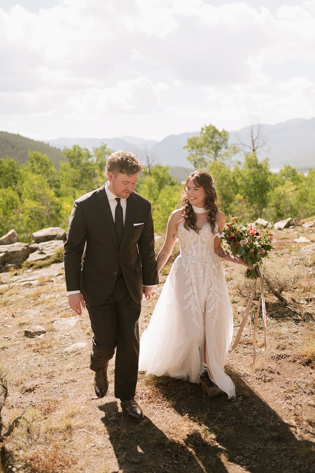 A bride and groom walking together outdoors in a mountainous landscape.